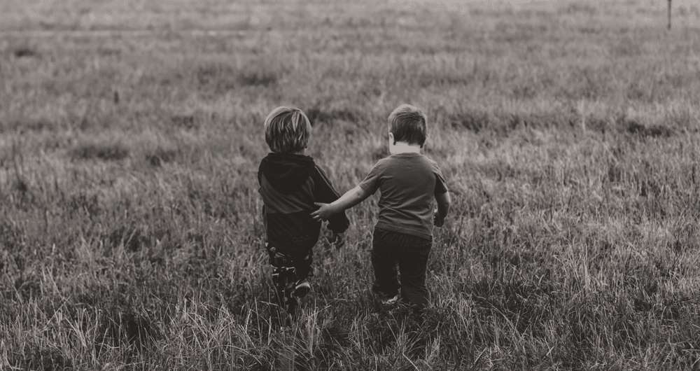 listen money matters - two boys walking in a grassy field