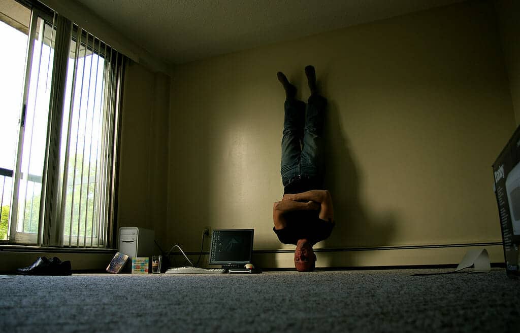 A man is standing on his head in a mostly bare room.