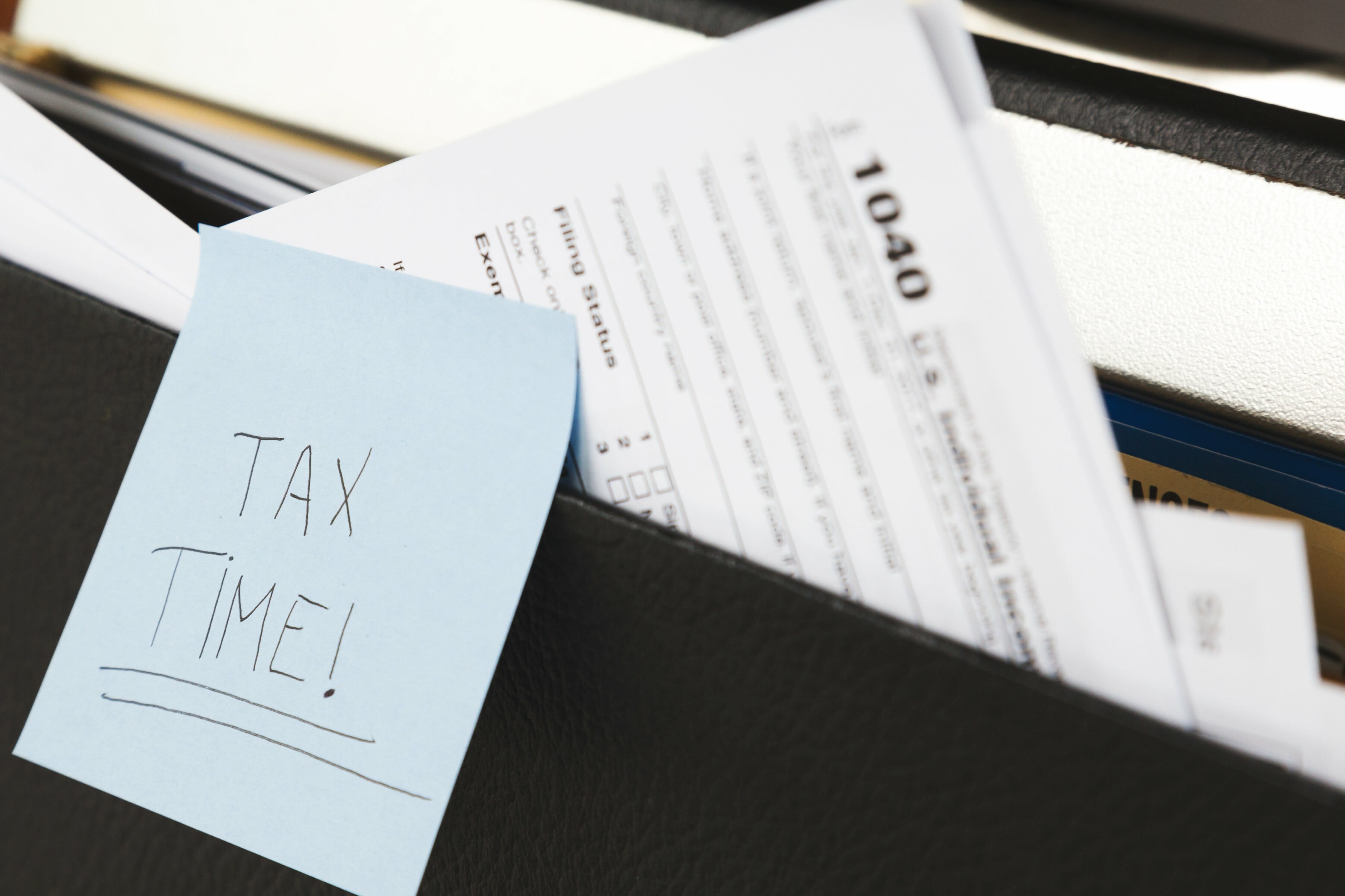 A folder with a 1040 tax form sticking out that has a sticky note that says "Tax time!"