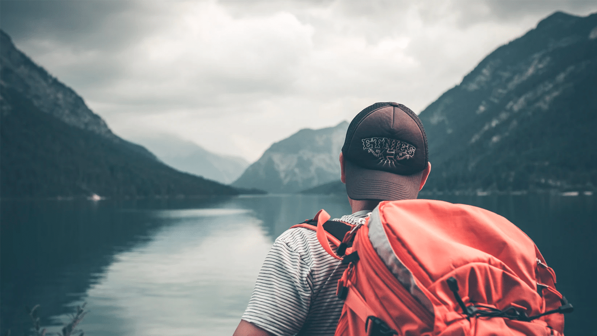 A backpacker looking out at the sight of a lake in the wilderness.